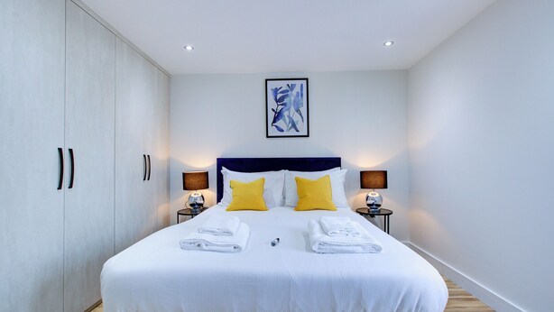 A modern hotel room with a large bed, two bedside lamps, and a framed artwork on the wall. - Hybrid Resi - Uxbridge|1 Bed Apartment (Uxbridge)