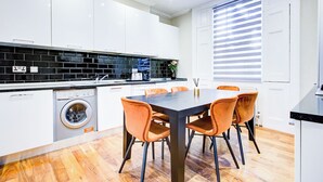 Eine moderne Küche mit weißen Schränken, einer schwarzen Fliesenrückwand, einer eingebauten Waschmaschine und einem Essbereich mit orangefarbenen Stühlen.