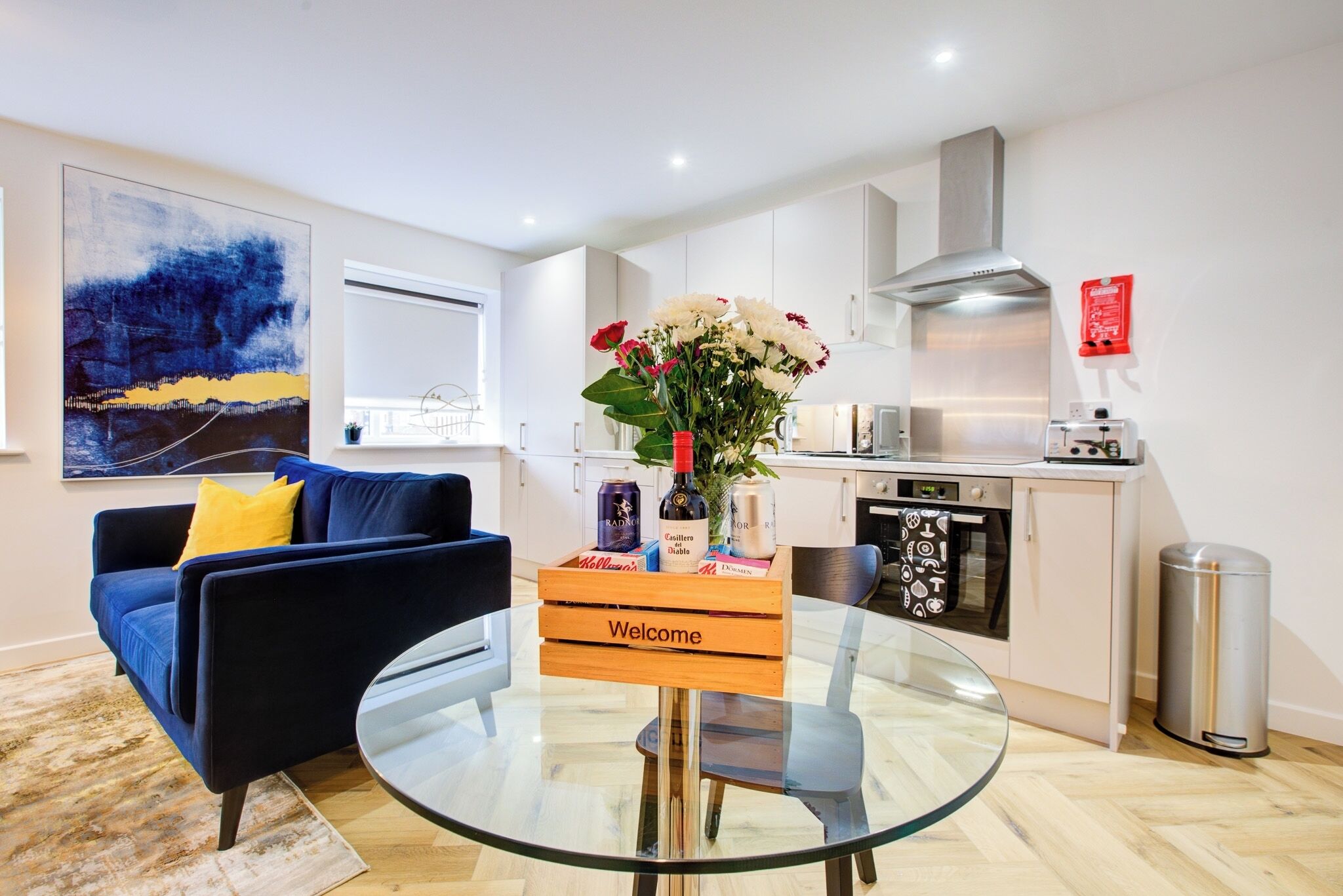A modern living room with a blue sofa, a glass coffee table, and a welcome sign.