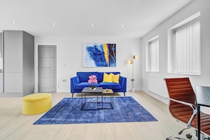 Uma sala de estar moderna com um sofá azul, um banquinho amarelo, uma mesa de centro e uma cadeira vermelha.