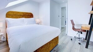 Ein modernes Hotelzimmer mit einem großen Bett, einem Schreibtisch mit Stuhl und einem Dachfenster.