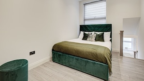 A bedroom with a green upholstered bed, white bedding, and a window with blinds.