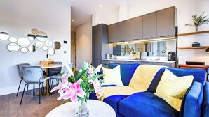 Uma sala de estar moderna com um sofá azul, uma mesa de centro com flores e uma área de jantar com mesa e cadeiras.