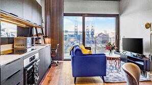 Um apartamento moderno com cozinha compacta, sala de estar com sofá azul, televisão e varanda com vista para a cidade.