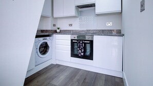 A compact kitchen with white cabinets, a built-in washing machine, and a microwave.