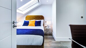 A modern hotel room with a bed, a side table, a chair, and a skylight.