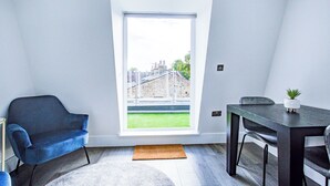 A modern room with a large window, a blue chair, a dining table with chairs, and a small plant on the table.