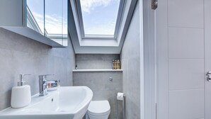 A modern bathroom with a skylight, a white sink, a toilet, and a shelf with toiletries.