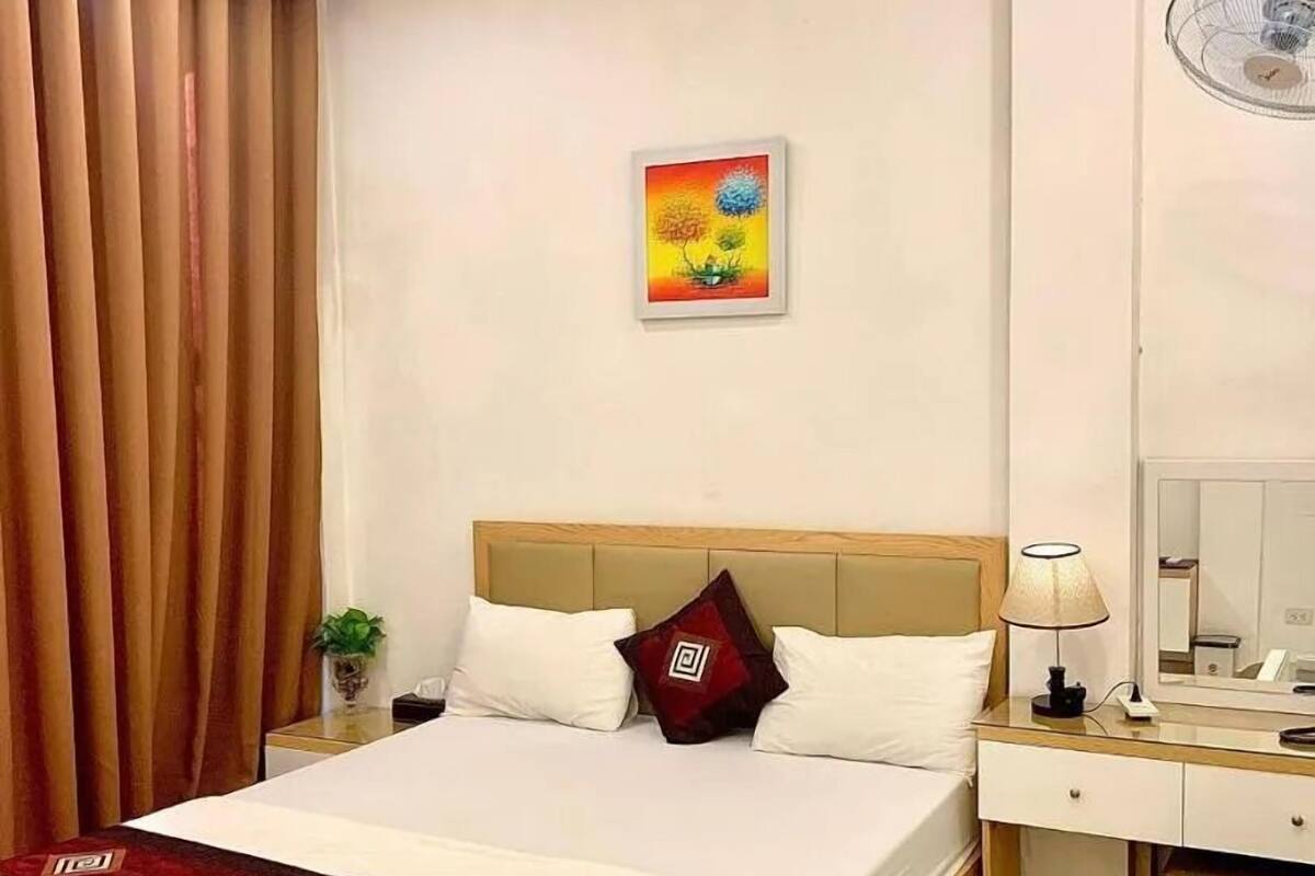 A hotel room with a bed, bedside table, lamp, mirror, and a painting on the wall.