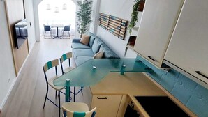 A modern kitchen with a dining area, featuring a built-in stove, a dining table with chairs, and a sofa.