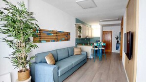 A modern living room with a blue sofa, a large potted plant, and a kitchen area with a dining set.