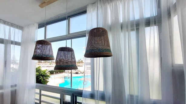 A balcony with wicker pendant lights, a pool view, and sheer white curtains.