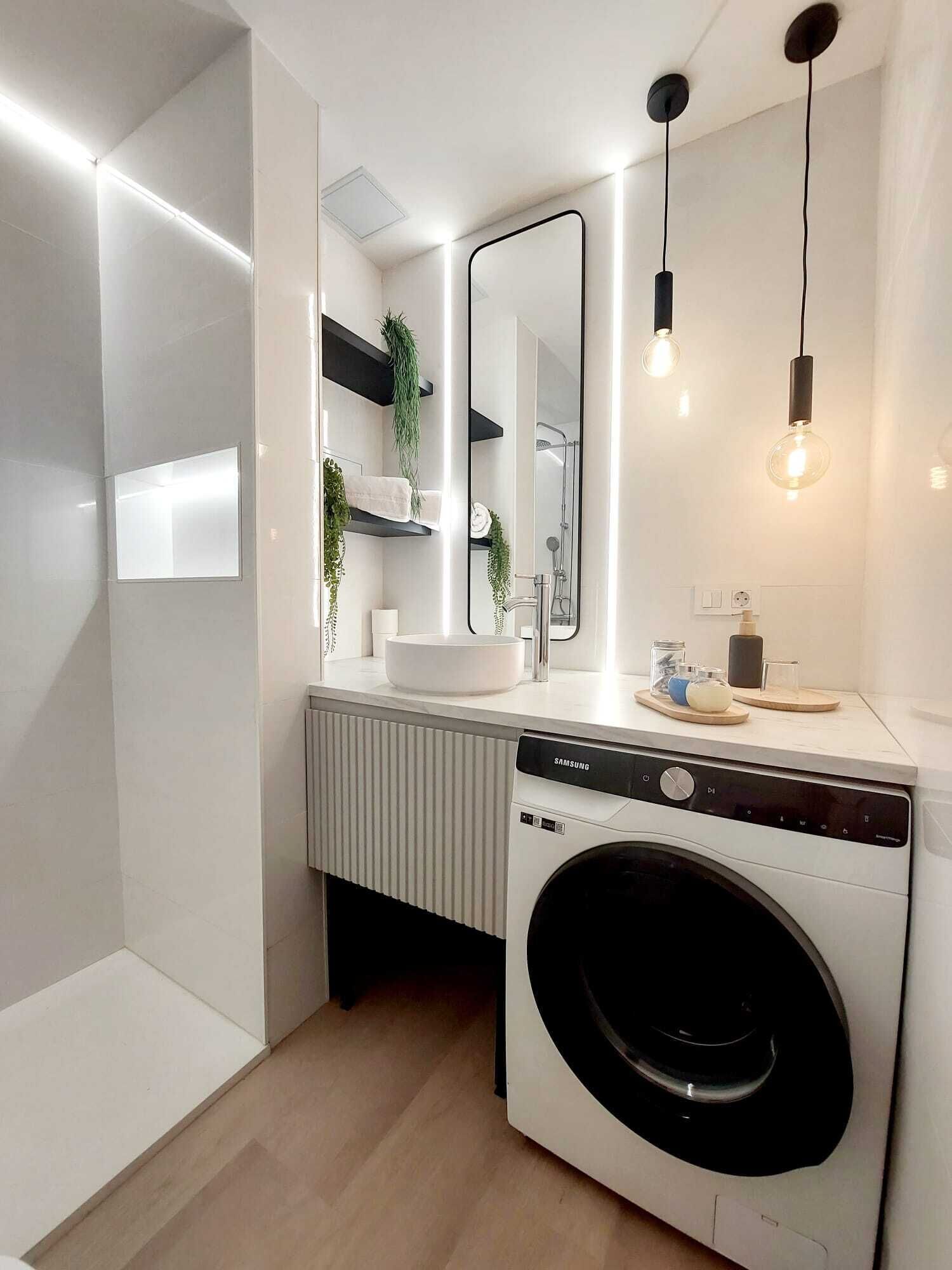 Een moderne badkamer met een ingebouwde wasmachine, een grote spiegel en hangende lampen.