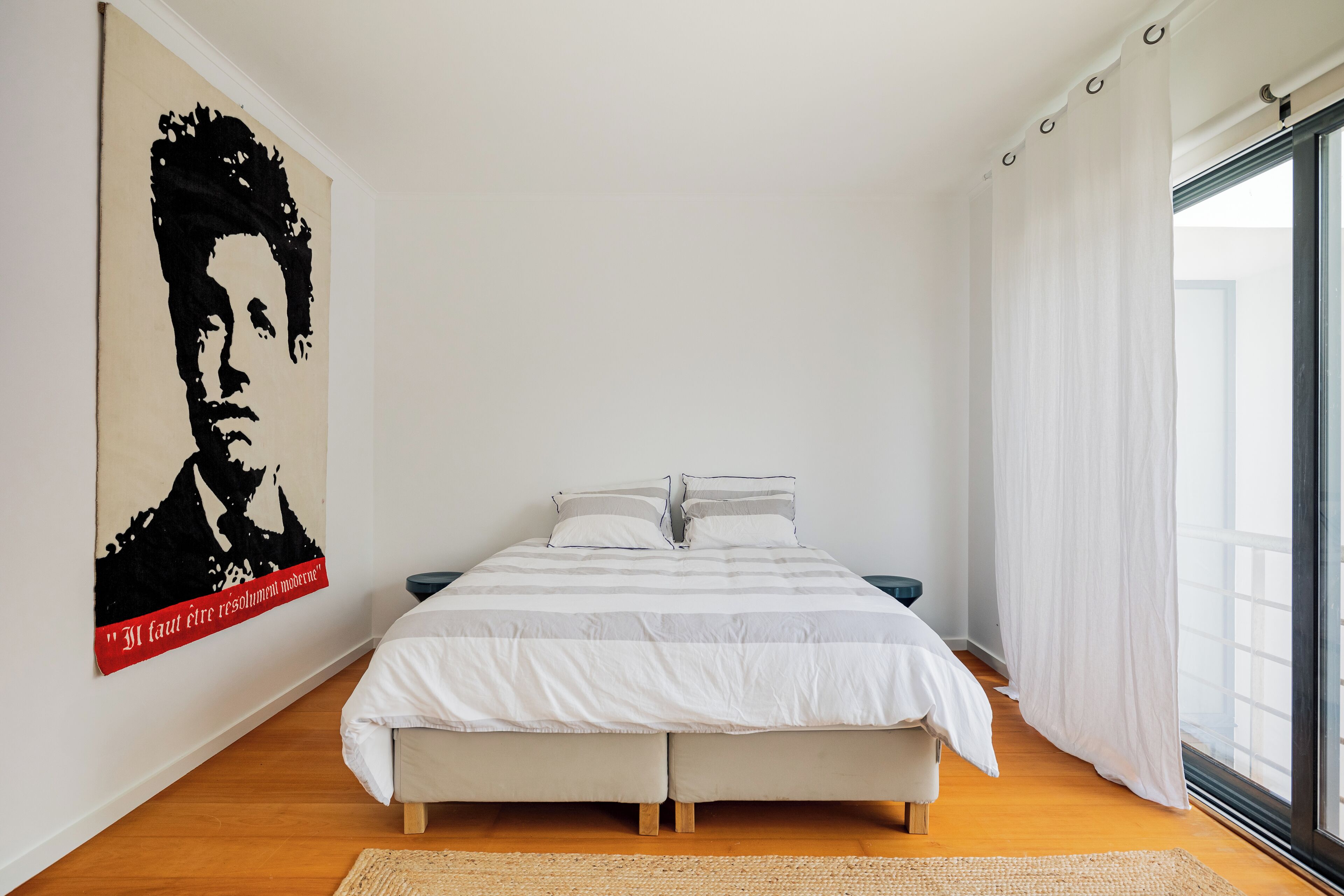 Un dormitorio con cama, un cartel en la pared y una ventana con cortinas.