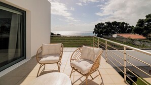 Un balcón con dos sillas de mimbre y una mesa, con vistas a la costa.