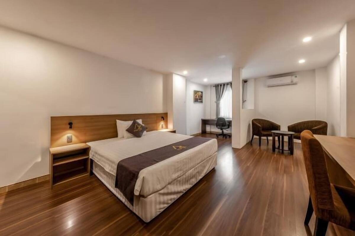 A hotel room with a bed, bedside table, desk, and two chairs.