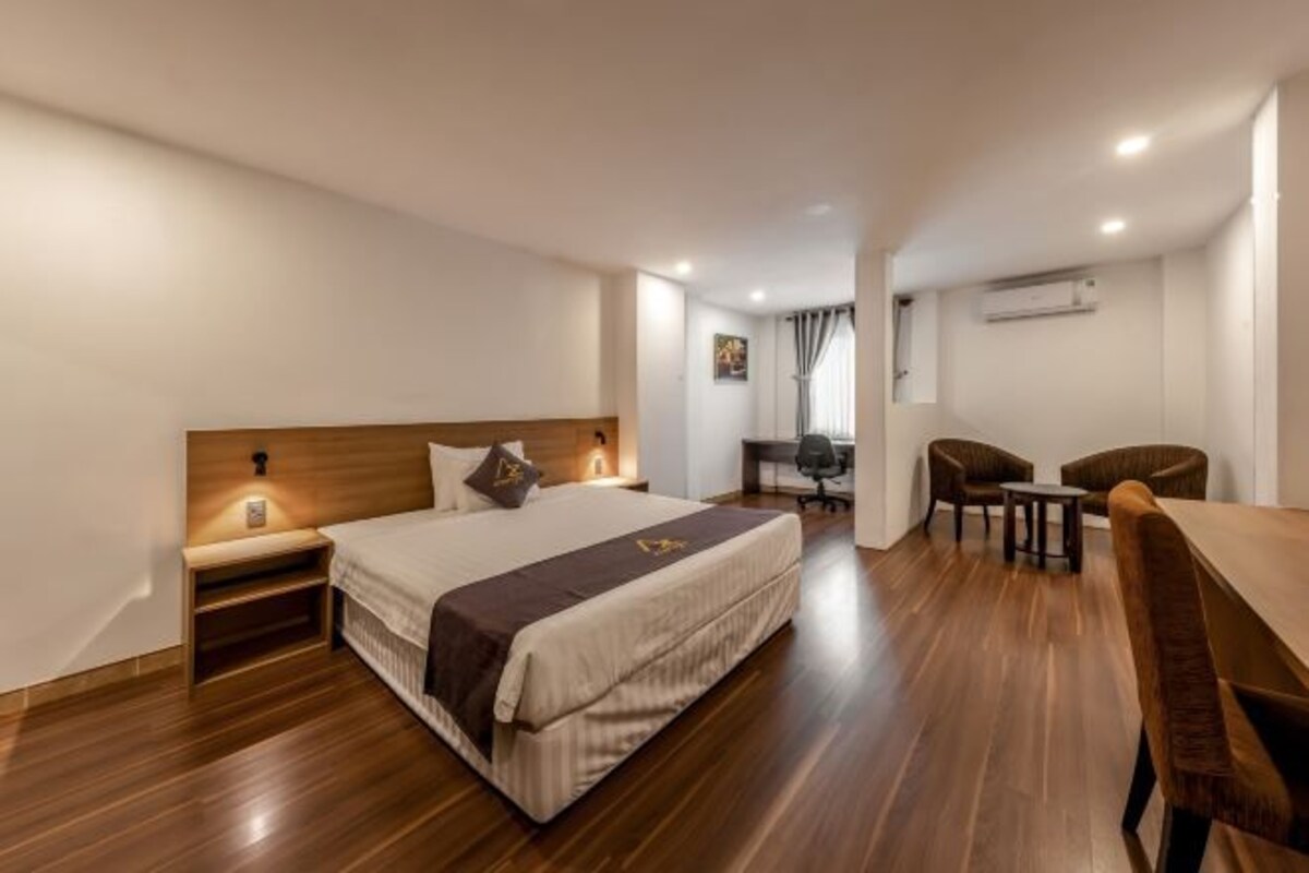 A hotel room with a bed, bedside table, desk, and two chairs.