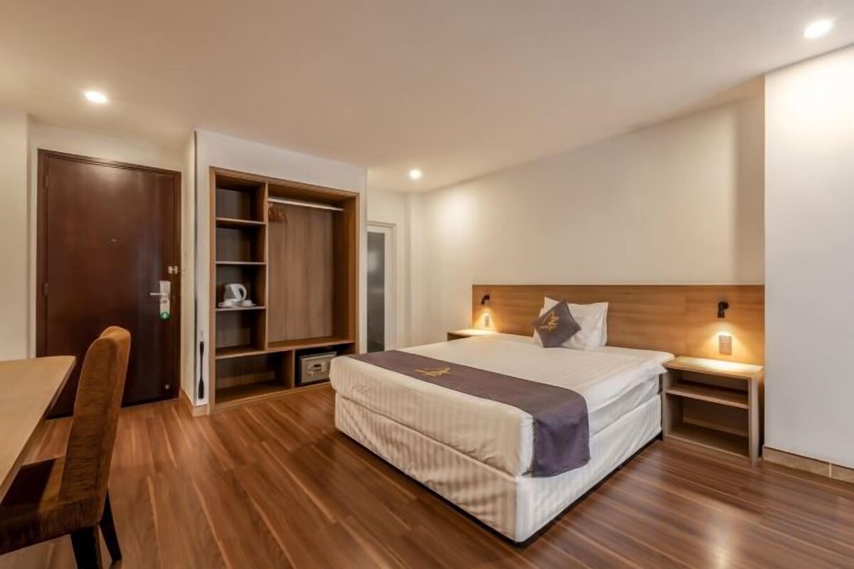 A bedroom with a bed, bedside table, nightstand, wardrobe, and a desk with a chair.
