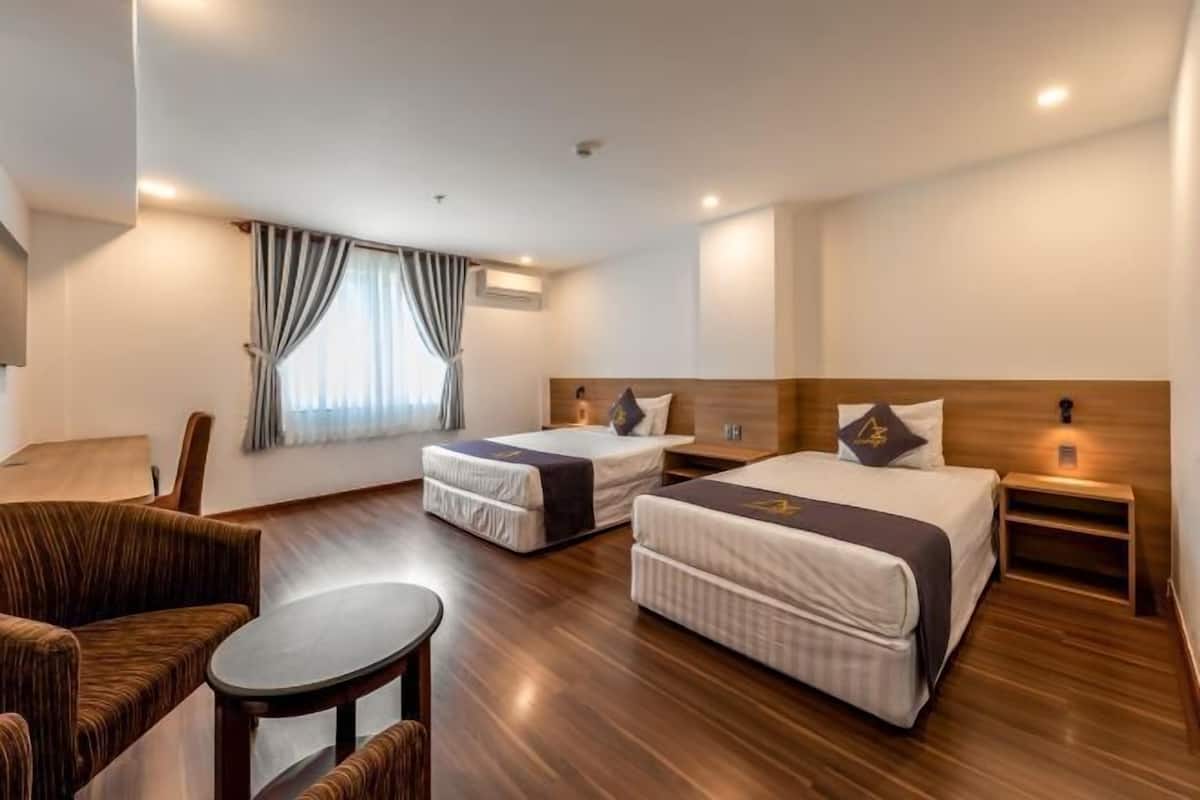 A hotel room with two beds, a sofa, a small table, and a window with curtains.