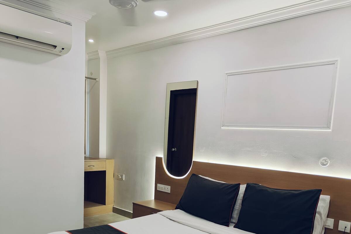 Une chambre d’hôtel avec un grand lit, un ventilateur de plafond, un appareil de climatisation, une table de chevet avec un téléphone et un miroir au mur.