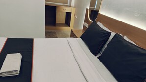 En snyggt bäddad säng med vita och svarta sängkläder, en hopvikt handduk och ett träbord vid sängen med en låda.