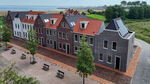 Una hilera de casas tradicionales y modernas con tejados rojos, una playa de arena y aerogeneradores al fondo.