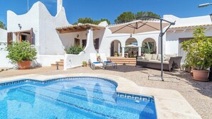 A pool area with a tiled pool, outdoor seating, and a white building with arches.