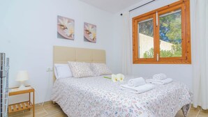 A bedroom with a bed, a nightstand, a window, and floral artwork on the wall.
