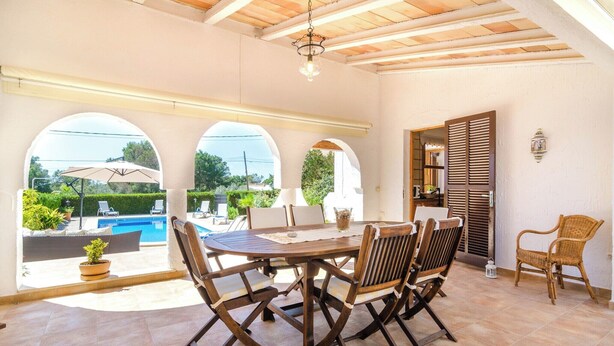 A patio with a round table and chairs, a pool, and a covered area with a view of the outdoors.