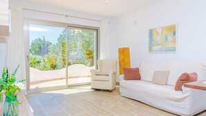 A modern living room with a white sofa, a beige armchair, and a large window with a view of greenery.
