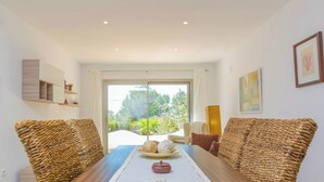 A dining area with a wooden table, wicker chairs, and a view of greenery through a glass door.