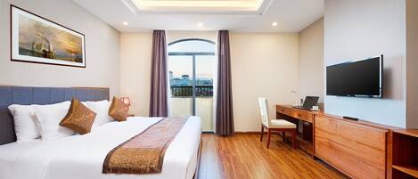 A hotel room with a bed, a desk, a television, and a view of the city through large windows.