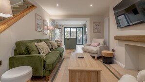 A modern living room with a green sofa, a white armchair, a wooden coffee table, and a staircase.