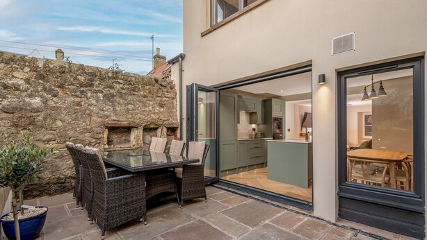 A modern house with a stone wall, a glass door leading to a kitchen, and a dining area with wicker furniture.