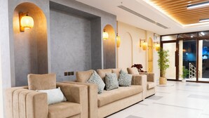 Un vestíbulo moderno con un sofá color beige, lámparas fijadas a la pared y un ventanal grande.