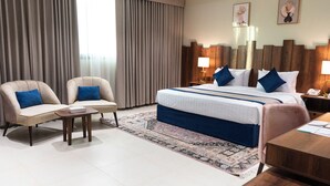 Una habitación de hotel con una cama grande, dos sillones, una mesita y un escritorio.