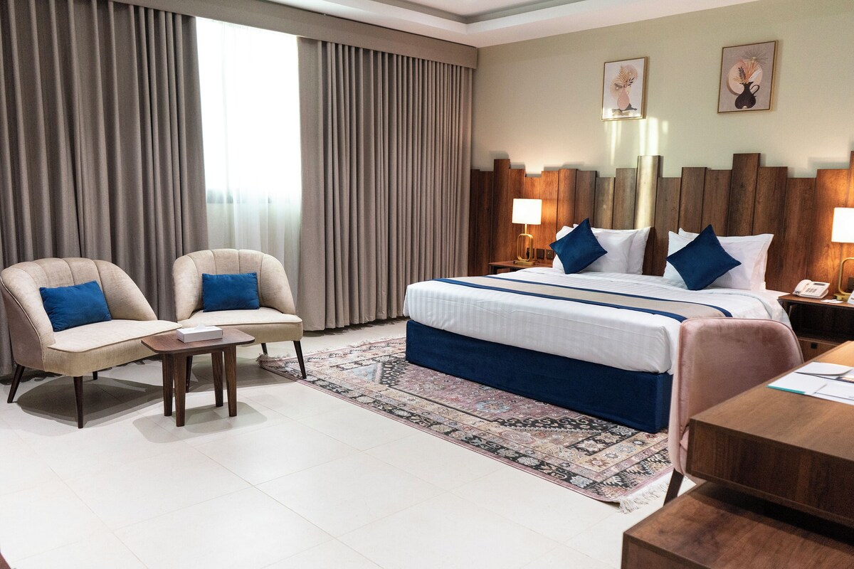 A hotel room with a large bed, two armchairs, a small table, and a desk.