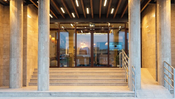 Una entrada de edificio moderna con grandes columnas, una puerta de cristal y una escalera que conduce al interior.