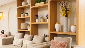 Una sala de estar moderna con un sofá color beige, estanterías de madera con adornos, y un jarrón grande con flores amarillas.