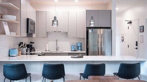A modern kitchen with a central island, stainless steel appliances, and black chairs. - Revelstoke - Alpine Retreat (Revelstoke)