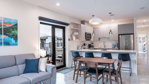 A modern kitchen with a central island, a dining area with a wooden table and chairs, and a living area with a sofa and a large window overlooking a balcony. - Revelstoke - Alpine Retreat (Revelstoke)