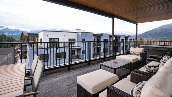 Ein Balkon mit Gartenmöbeln, Blick auf ein Gebirge und moderne Gebäude im Hintergrund.