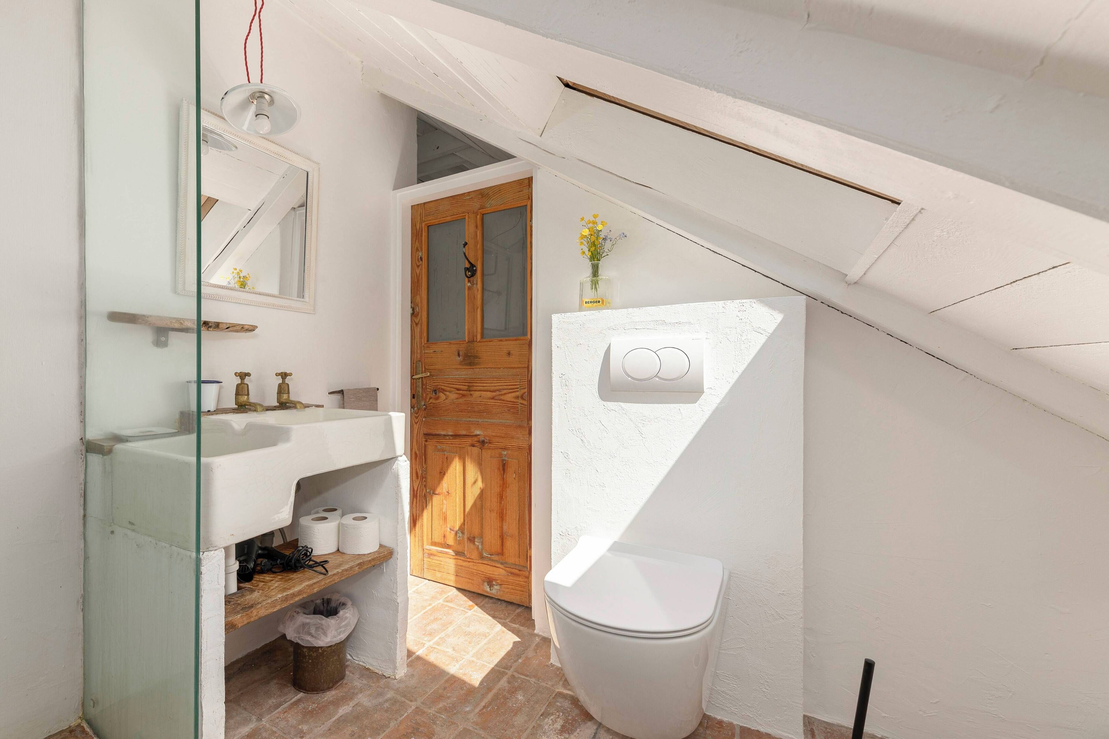 Een kleine, praktische badkamer met een wit wastafel, een houten deur en een wit toilet.