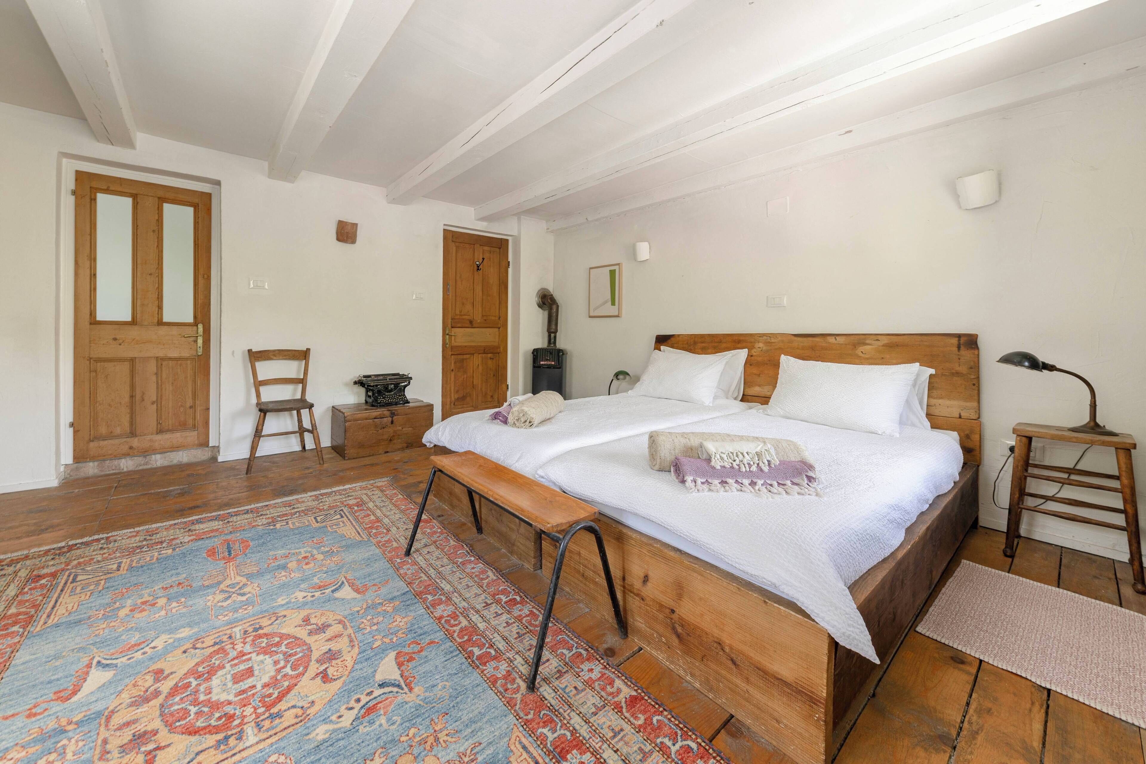 Une chambre à coucher avec un lit en bois, un banc, un tapis et une cheminée.