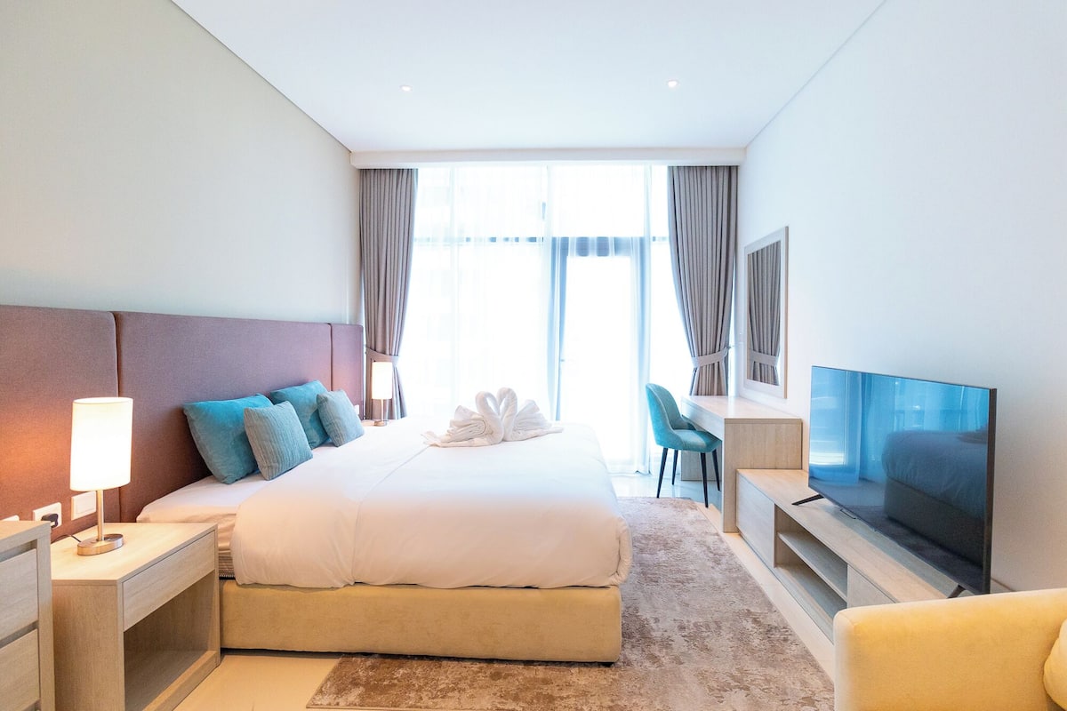 A modern hotel room with a large bed, a desk, a television, and a view of the outdoors.