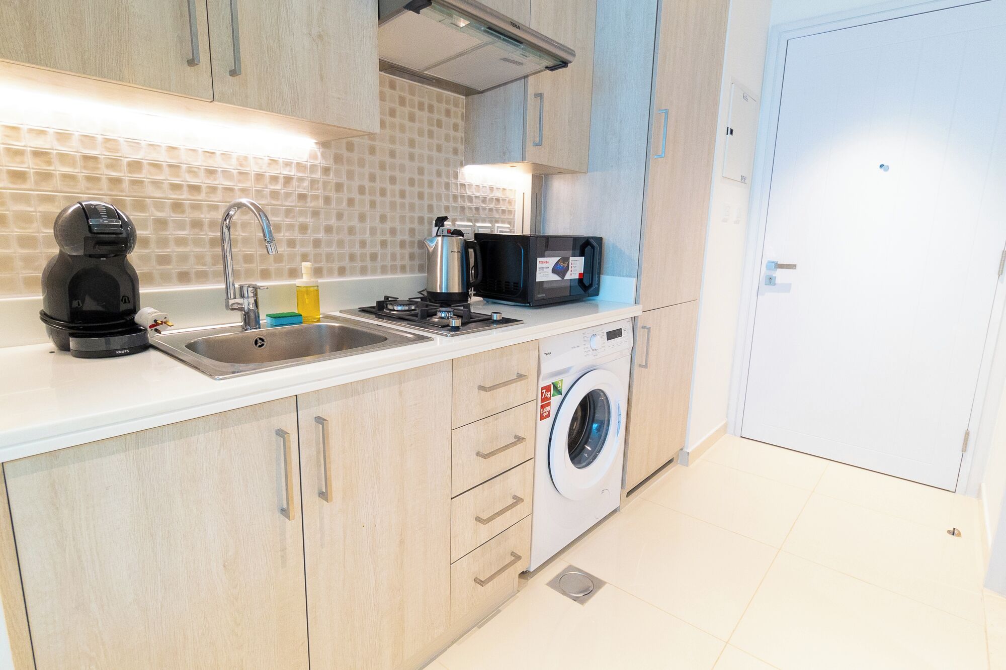 Cocina compacta con lavamanos, cafetera, microondas y lavadora.