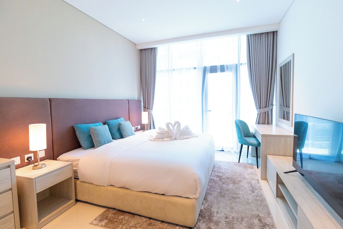 A hotel room with a bed, a desk, a chair, a TV, and a window with curtains.