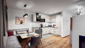 Una cocina moderna con armarios blancos, un comedor con mesa y sillas de madera, y un sofá gris con cojines rojos.