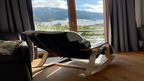 Una sala de estar moderna con una mecedora, un sofá y vistas a un paisaje montañoso a través de amplias ventanas.