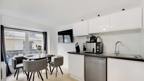A modern kitchen with white cabinets, a stainless steel dishwasher, and a built-in microwave. There is a dining table with two chairs and a window with curtains. - Appartement in the heart of Paris ☆ Opera ☆ (Paris)